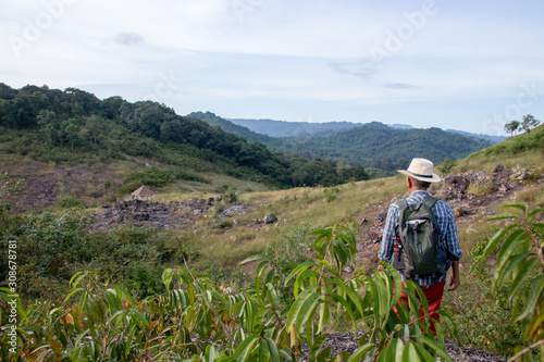 An Asian old man is searching for a path and a mountain to climb during the holidays with good weather. He comes with a backpack to use to rest on the way. Relax by the good weather and freedom.
