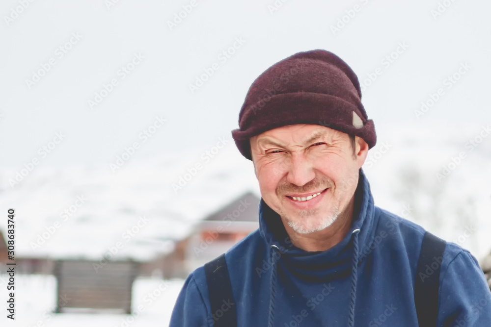 Adult smiling man chopping wood with an ax near his wooden house in the village Adult smiling man chopping wood with an ax near his wooden house in the village