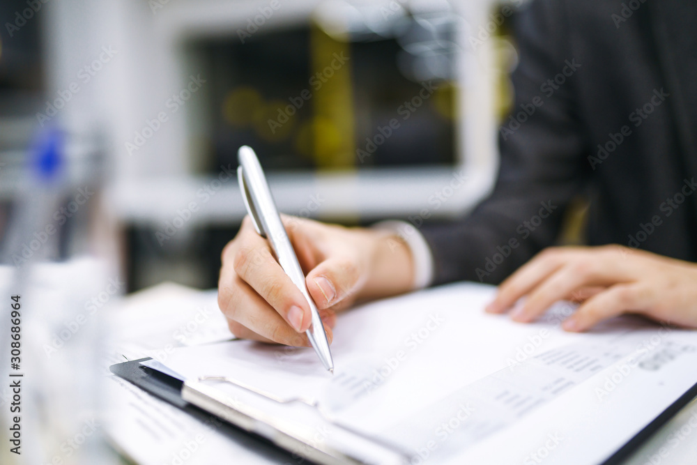 Fototapeta premium A man signs a contrac, legal or business agreements. Male hand with pen of young office worker makes notes. Business man sitting at office desk and signing a document in modern office.