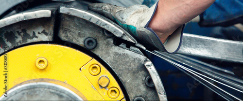 Worker`s hands with a metal stake against a manufacturing machine for slitting/cutting/stripping steel sheets
