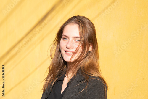Fotografie Attarctive smiling brunette girl with blue eyes in black cloak, yellow wall on t