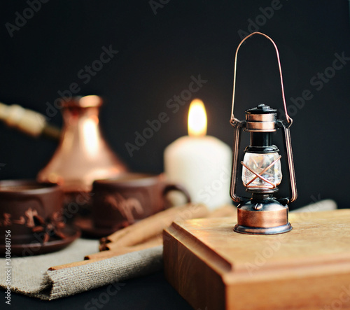 decorative small lanterm on a wooden stand, cinnamon sticks, caps of coffee, candle, canvas napkin on a dark background, close-up photo