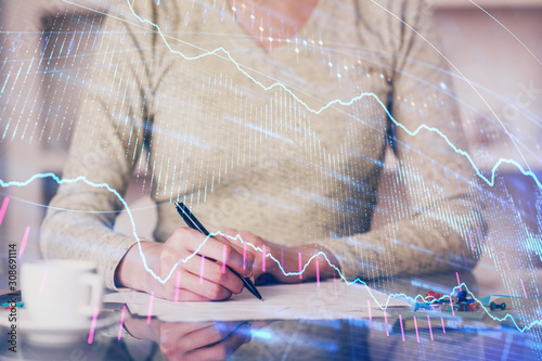 Hand taking notes in notepad. Forex chart holograms in front. Concept of research. Double exposure