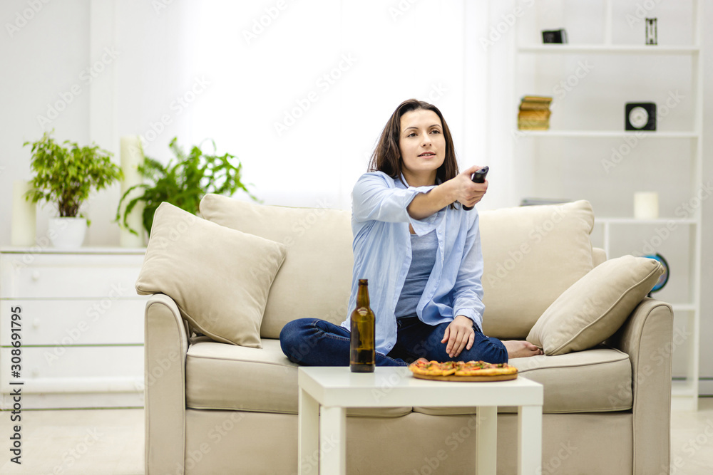 Adorable brunette woman is switching on TV with a zapper and is ready to engulf junk food. Adorable brunette woman is switching on TV with a zapper and is ready to engulf junk food.