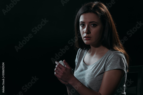 frustrated woman looking at camera while going to commit suicide and holding container with pills isolated on black