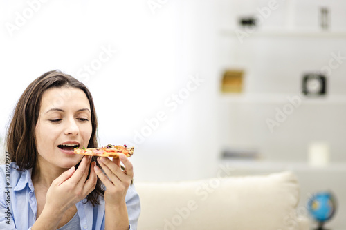 Attractive brunette woman wants to eat pizza slice, looking at it, on light background. Close up. Copy space.