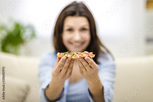 Blurred smiling woman is presenting hot  delicious slice of pizza. Close up. Copy space.