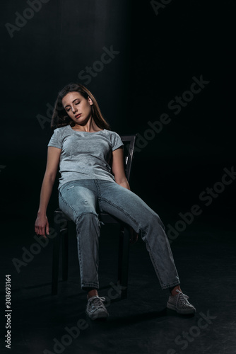 young, lifeless woman on chair after committing suicide on black background