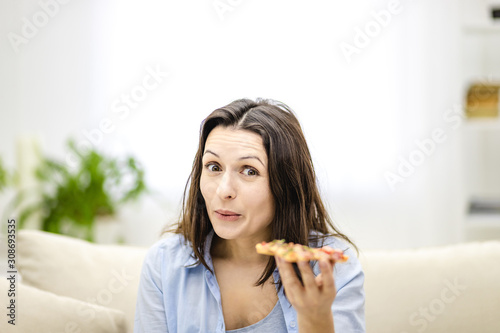 Brunette woman is positively shocked how tasty pizza is, and raises her eyebrows up. Closed up.