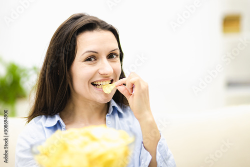 Happy adorable brunette women offers a large deep plate with potato chips snack. She is tasting snack. Close up.