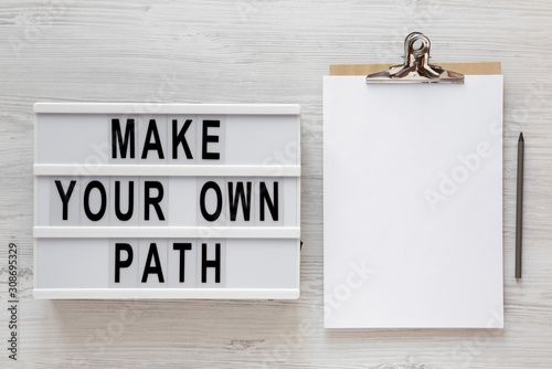 'Make your own path' words on a modern board, clipboard with blank sheet of paper on a white wooden surface, top view. Overhead, from above, flat lay. Copy space. photo