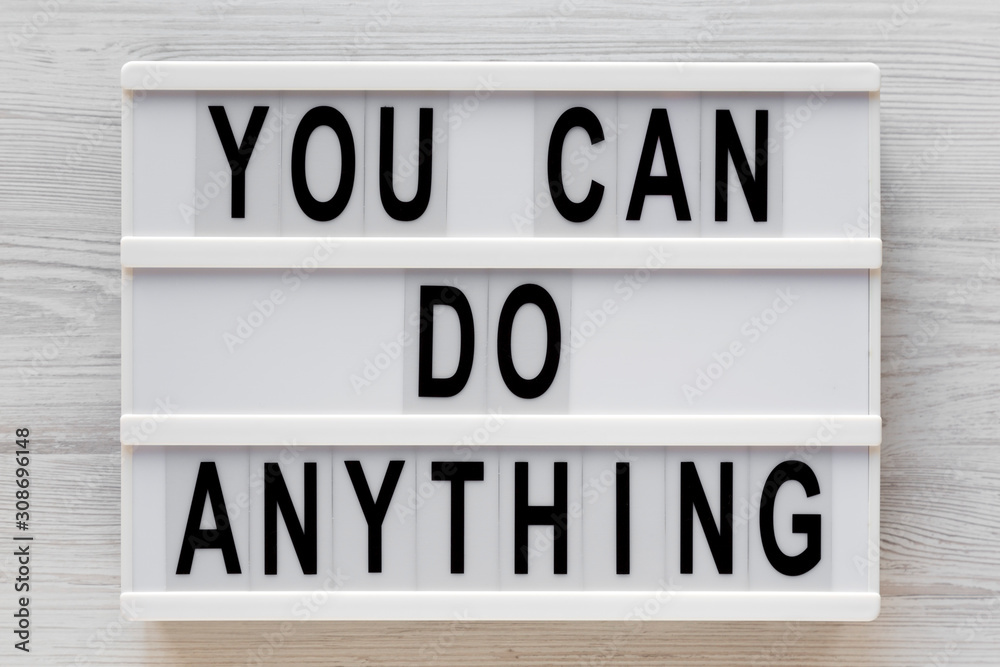 Fototapeta premium 'You can do anything' words on a modern board on a white wooden background, top view. Overhead, from above, flat lay. Close-up.