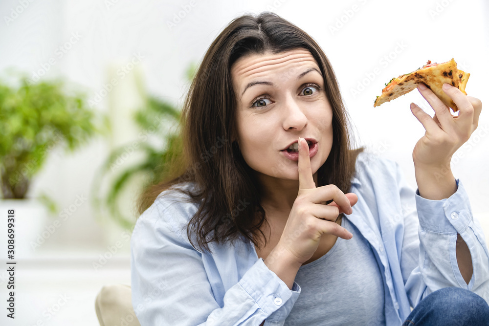 Beautiful young woman wants to eat pepperoni pizza slice so bad. But, she is on diet. So, she makes a silent gesture, for nobody to find out about her cheat. Beautiful young woman wants to eat pepperoni pizza slice so bad. But, she is on diet. So, she makes a silent gesture, for nobody to find out about her cheat.