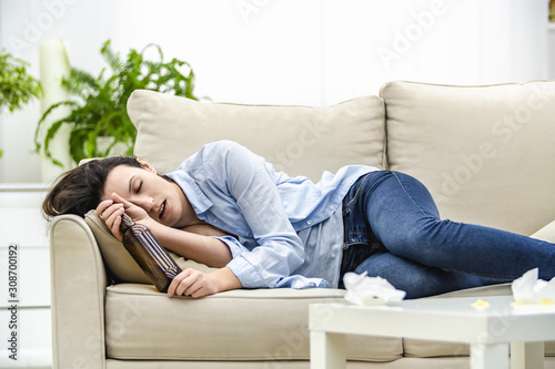 Unconscious drunk woman with empty bottle in her hand is lying on the sofa. Woman feels headache.