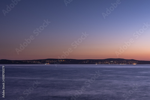 a long exposure photograph taken towards the end of golden hour looking south across a calm St Ives Bay at the Street lights lighting up St Ives
