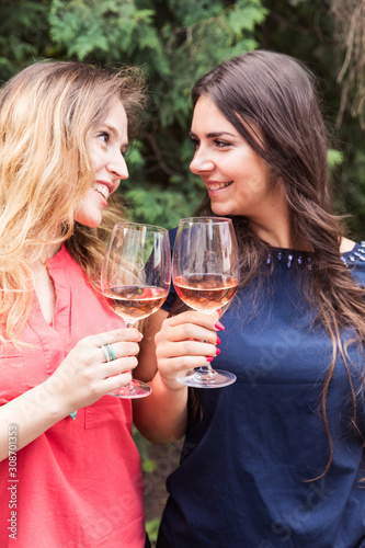 Two happy girls enjoying in a glass of wine and talking.