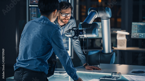 Diverse Team of Engineers Analyse and Discuss How a Futuristic Robotic Arm Works and Moves a Metal Object. They are in a High Tech Research Laboratory with Modern Equipment.