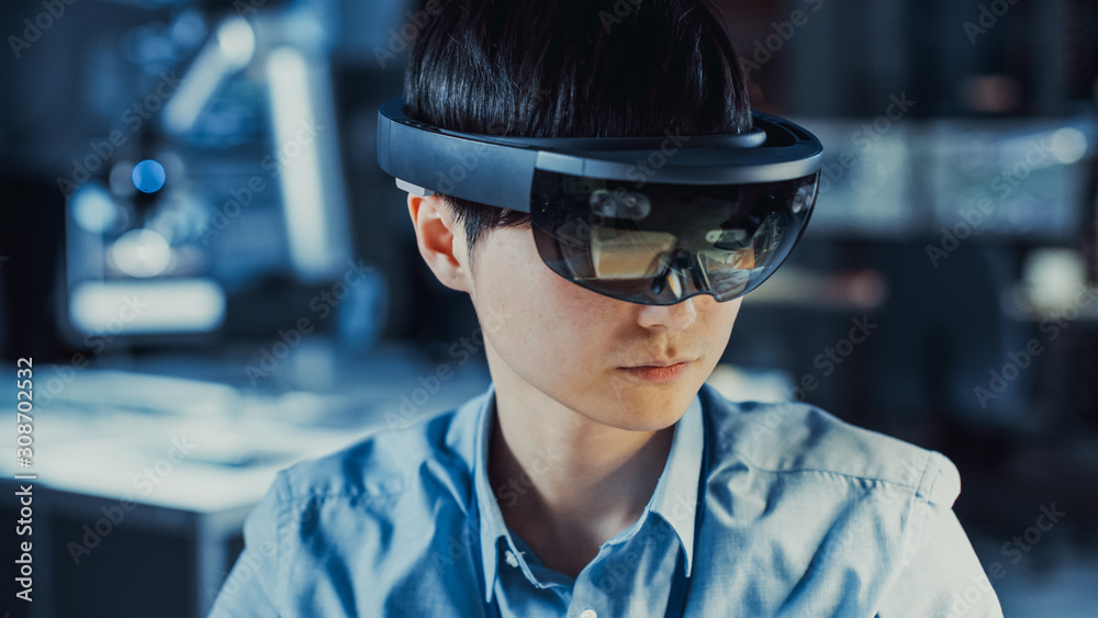 Professional Japanese Electronics Development Engineer in Blue Shirt is Wearing a Virtual Reality Headset and Looking Around the High Tech Research Laboratory with Modern Computer Equipment. Professional Japanese Electronics Development Engineer in Blue Shirt is Wearing a Virtual Reality Headset and Looking Around the High Tech Research Laboratory with Modern Computer Equipment.
