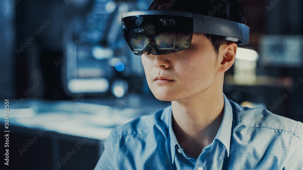 Professional Japanese Electronics Development Engineer in Blue Shirt is Wearing a Virtual Reality Headset and Looking Around the High Tech Research Laboratory with Modern Computer Equipment. Professional Japanese Electronics Development Engineer in Blue Shirt is Wearing a Virtual Reality Headset and Looking Around the High Tech Research Laboratory with Modern Computer Equipment.