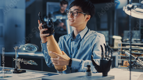 Futuristic Prosthetic Robot Arm Being Tested by a Professional Japanese Development Engineer in a High Tech Research Laboratory with Modern Computer Equipment. He is Satidfied with the Result. photo