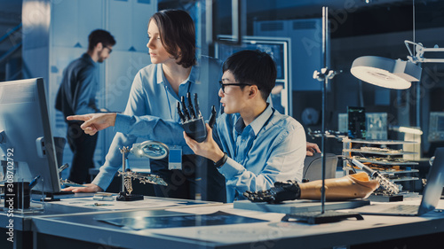 Technological Prosthetic Robot Arm is Tested by Two Professional Development Engineers in a High Tech Research Laboratory with Modern Futuristic Equipment. Man and Female Compare Data on a PC