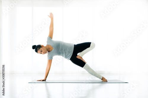 Asian Woman in side plank, Vasisthasana exercise. working out,full length, in white yoga studio ,concept of healthy life and natural balance, Side view photo