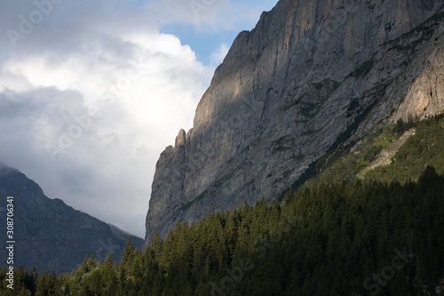 View on the valley and rock wall. Sunbeam behind the clouds. Forest below. High alpine mountains cloud scape. Switzerland.