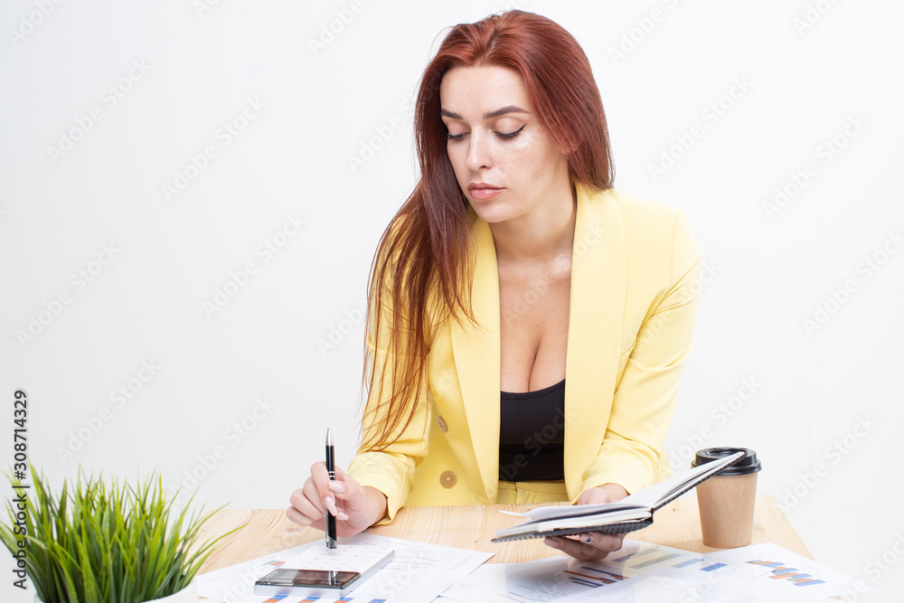 A red haired girl in a yellow business suit sits at a table and counts on a calculator A red haired girl in a yellow business suit sits at a table and counts on a calculator