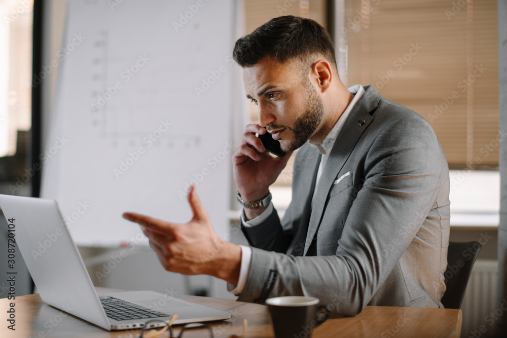 Handsome businessman in office talking on phone. Successful man in suit discussing business on phone call. 