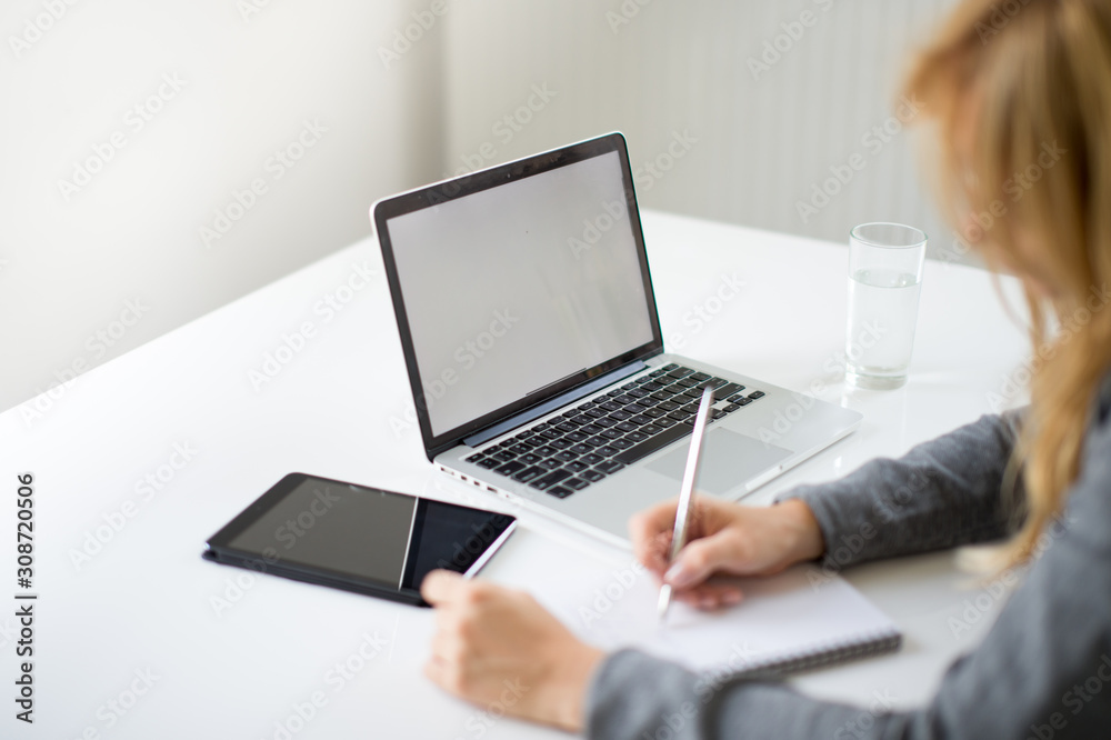 A blonde hair businesswoman working in her workstation. Businesswoman working at the desk at workplace. Woman working in home office. Woman sitting at desk and working with laptop and glass of water. A blonde hair businesswoman working in her workstation. Businesswoman working at the desk at workplace. Woman working in home office. Woman sitting at desk and working with laptop and glass of water.