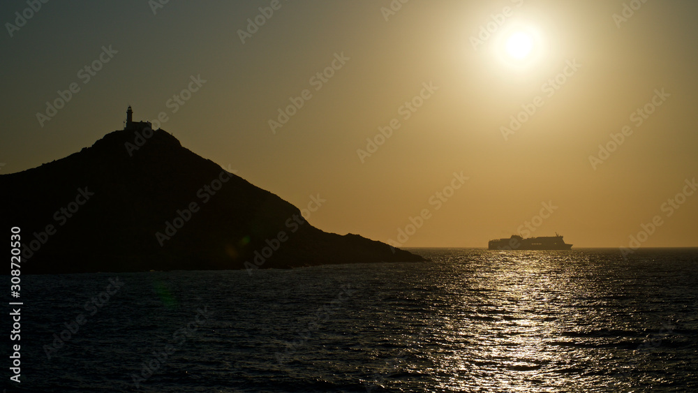 Spectacular sunset with endless horizon and sparkling waves. Lighthouse and rocky hills in the background.