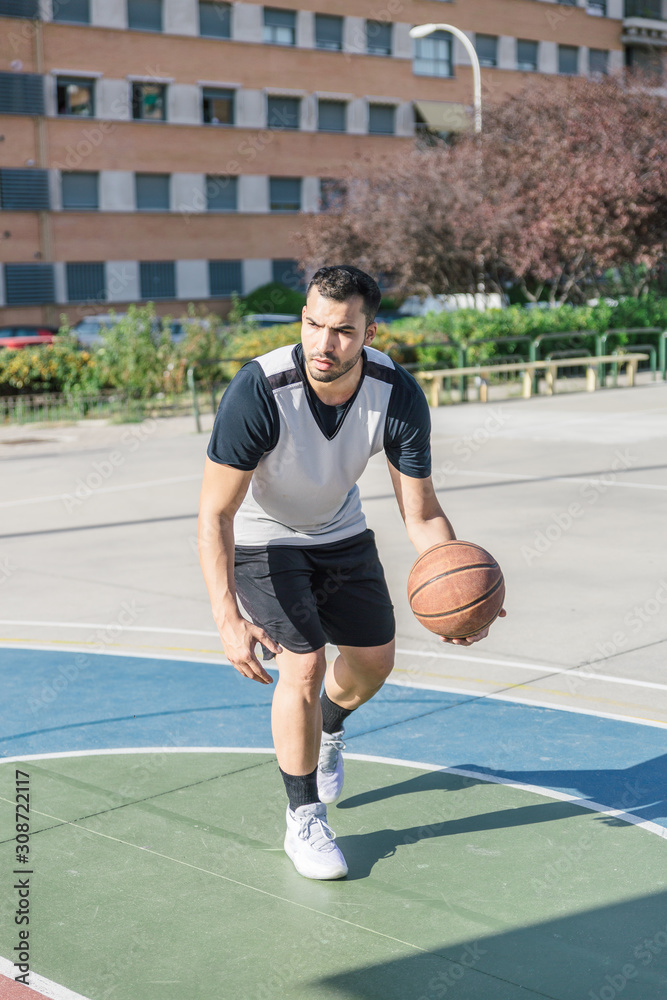 Basketball player moves his ball with his left arm while playing on an urban basketball court