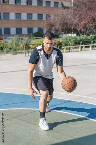 Basketball player moves his ball with his left arm while playing on an urban basketball court © Óscar