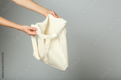 Female hand holding white cotton eco bag on grey background