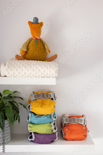 five colored washable diapers stacked on a shelf with a plush and a blanket, vertical