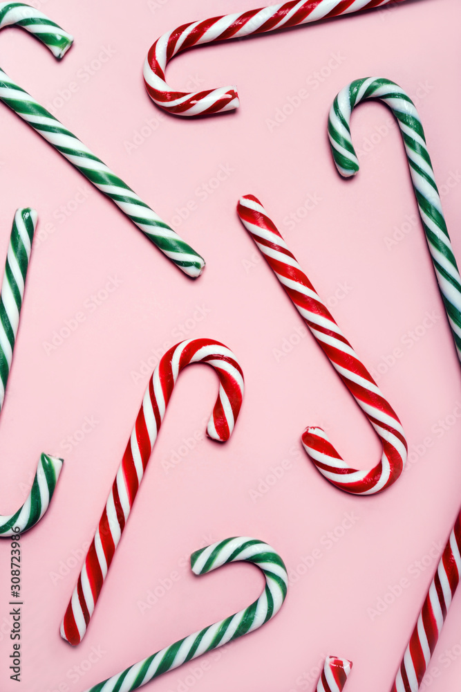 A scattering of red and green striped Christmas candy canes on a pink pastel warm background. New Year seamless pattern, top view. Flat lay. Vertical format