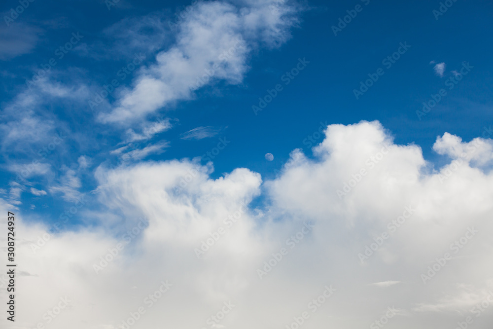 Fototapeta premium Background of white cumulus clouds with moon on a blue sky at daylight. Telephoto zoom shoot
