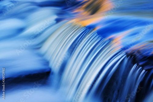 Bond Falls cascade captured with motion blur and illuminated by reflected color from sunlit autumn maples and blue sky overhead, Michigan's Upper Peninsula, USA 