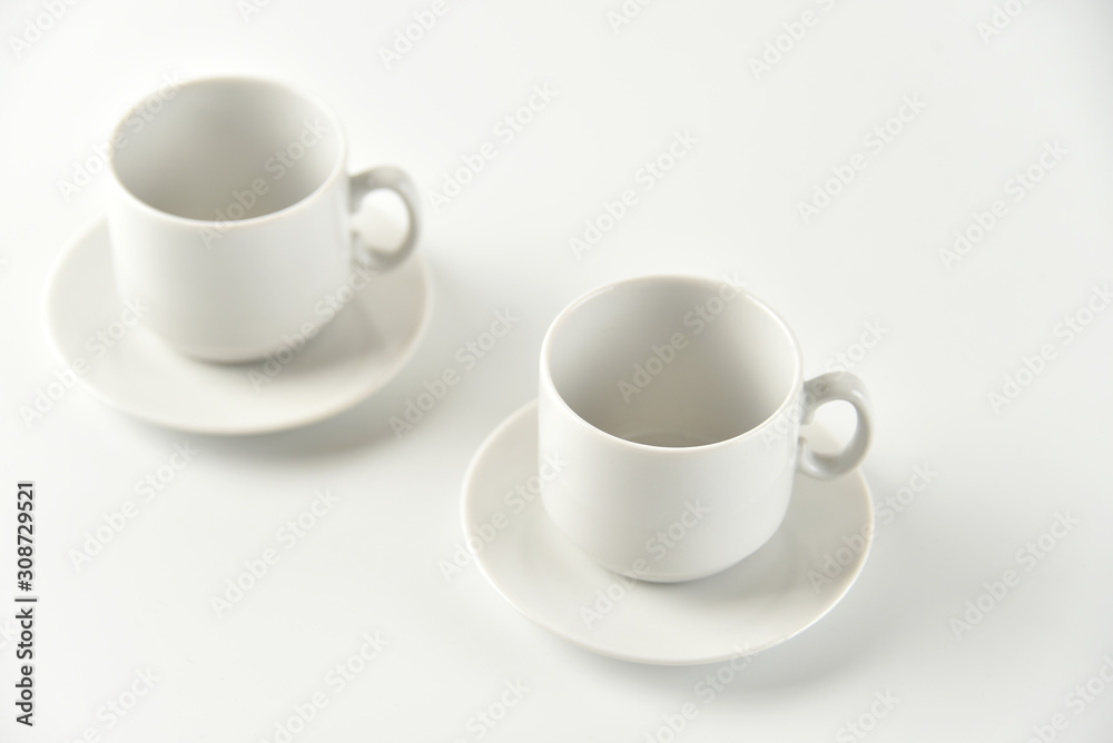 Two white empty cups and saucers on a white background. Selective focus. Two white empty cups and saucers on a white background. Selective focus.