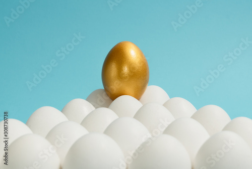 Concept of individuality, exclusivity, better choice. One golden egg among white eggs on blue background. photo
