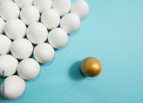 Concept of individuality  exclusivity  better choice. One golden egg among white eggs on blue background.