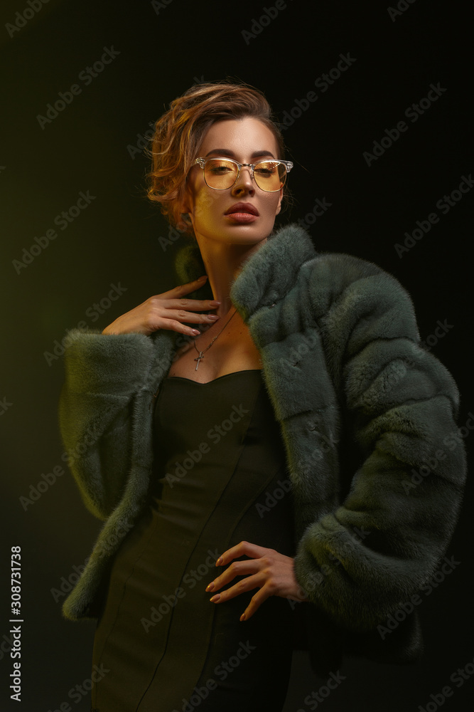 Portrait of a spectacular girl in yellow glasses jewelry and a fur coat made of natural fur.