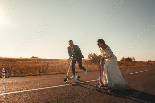 Smiling wedding couple riding a on scooters along the road outside the city at sunset. Place for text or advertising