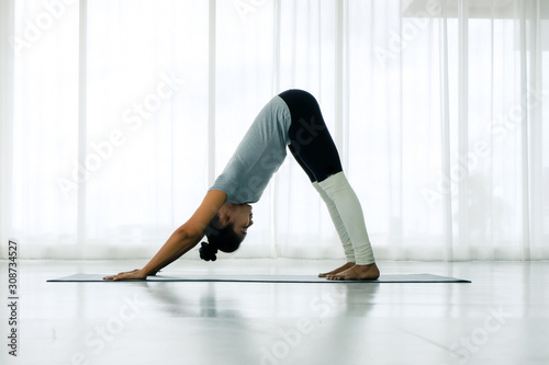 Beautiful Asian woman doing yoga exercise in the white room, downward facing dog pose, adho mukha svanasana (sun salutation pose), full length, Concept of healing body and spirit.side view
