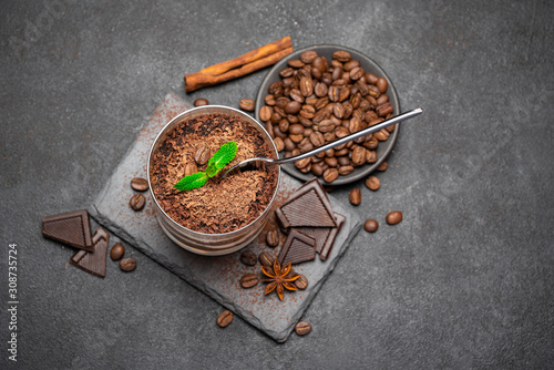Classic tiramisu dessert in a glass cup and pieces of chocolate on stone cutting board on darl concrete background photo