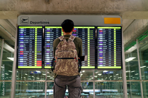 Young man with backpack looking at blurry flight information display screen at the airport