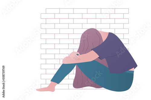 Depressed or upset girl sitting by the brick wall.