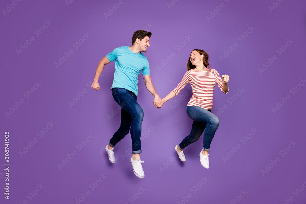 Full body profile photo of crazy funky two people guy lady jumping high rushing season sales black friday wear casual blue striped t-shirts jeans shoes isolated purple color background Full body profile photo of crazy funky two people guy lady jumping high rushing season sales black friday wear casual blue striped t-shirts jeans shoes isolated purple color background