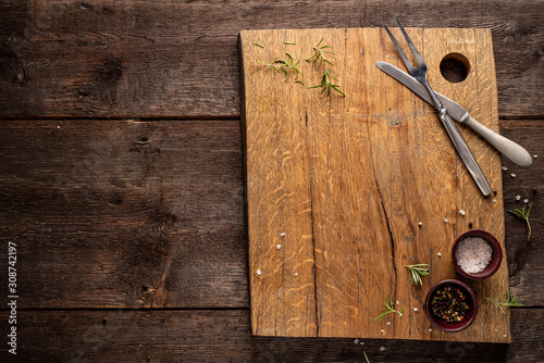 Chopping board on dark, wooden table. Rosemary, pepper, salt. Copy space.