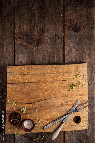 Chopping board on dark, wooden table. Rosemary, pepper, salt. Copy space.